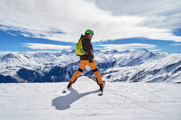 Man skier smiling and posing with a beautiful winter mountain panorama in Les Sybelles ski domain, France, on a sunny day with blue sky and white clouds.