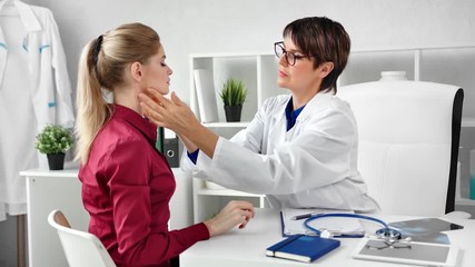 Professional female doctor checking patient neck examining glands at modern clinic white interior