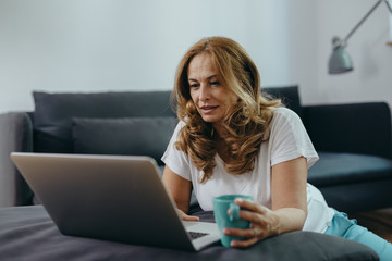middle aged woman using laptop computer and drinking coffee at her home