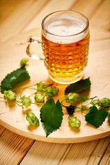 Large pint of beer with foam and sprigs of hops on wooden table