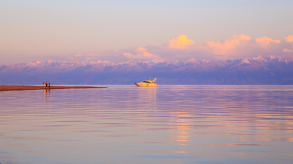 White yacht on the water in the rays of the setting sun. Kyrgyzstan, Issyk-Kul Lake. Bright sky, background in warm colors.