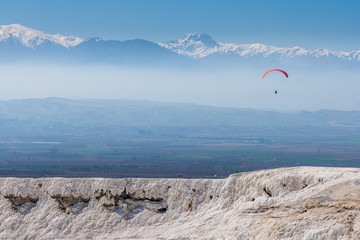 Paraglider flying over white terraces in Pamukkale, Denizli - Turkey. Cotton castle in southwestern Turkey.