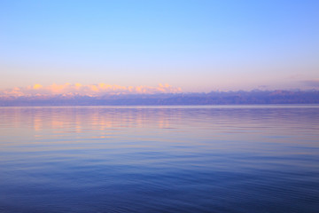 Beautiful sunset on a lake in the mountains. Kyrgyzstan, Issyk-Kul Lake. Bright sky, background in warm colors.