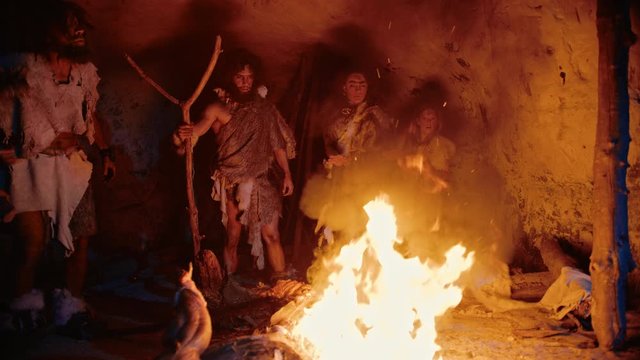 Tribe of Prehistoric Hunter-Gatherers Wearing Animal Skins Stand Around Bonfire Outside of Cave at Night. Portrait of Neanderthal / Homo Sapiens Family Doing Pagan Religion Ritual Near Fire