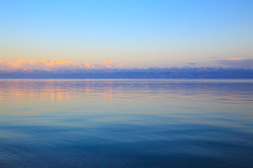 Beautiful sunset on a lake in the mountains. Kyrgyzstan, Issyk-Kul Lake. Bright sky, background in warm colors.