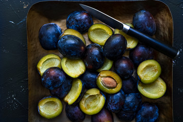 Top down view of sliced fresh blue plums and knife on a metal tray