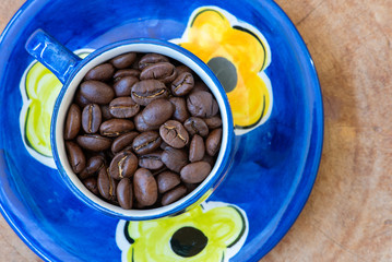Coffee beans in a hand-painted cup and saucer arranged on a wooden background.