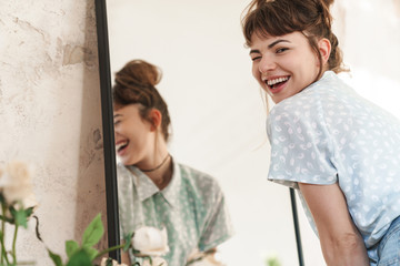 Emotional happy beautiful woman indoors at home posing near mirror looking camera.