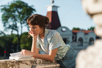 Concentrated young beautiful woman reading book on a balcony.