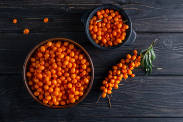 Sea buckthorn in two bowls, one branch on a dark wooden background