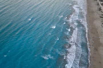 Fototapeta premium White foamy sea waves splash to sandy beach in the evening. Evening surf. Aerial top view from UAV drone
