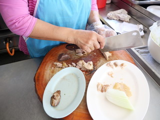 Middle-aged Asian women chopped boiled chicken meat on a wooden chopping board, Cooking for sale in the chicken rice shop in Thailand