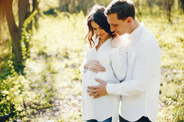 bright and happy pregnant woman walking in the park with her husband