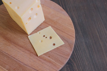 Cheese with holes lies on a wooden board on a brown table.