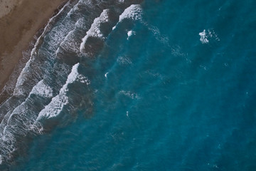 White foamy sea waves splash to deserted sandy beach in the evening. Evening surf. Aerial top view from UAV drone