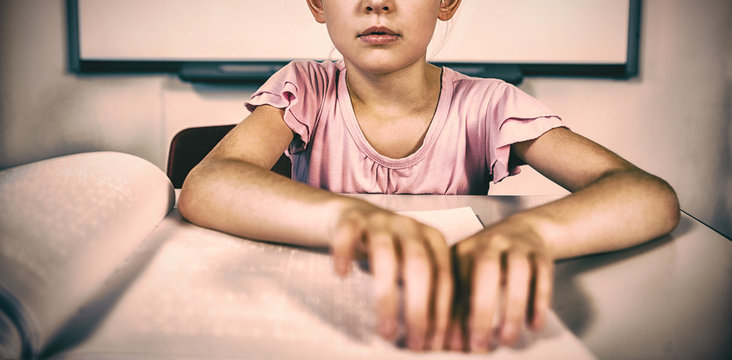 Schoolgirl reading a braille book in classroom