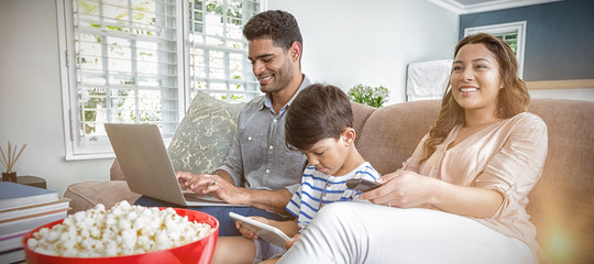 Mother watching television while father and son using laptop and digital tablet