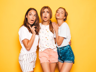 Three young beautiful smiling hipster girls in trendy summer clothes. Sexy carefree women posing near yellow wall in studio. Positive models going crazy and having fun.Hugging