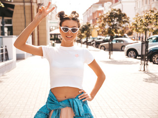 Beautiful smiling model with horns hairstyle dressed in summer hipster jacket jeans clothes.Sexy carefree girl posing in the street background.Trendy funny and positive woman having fun in sunglasses