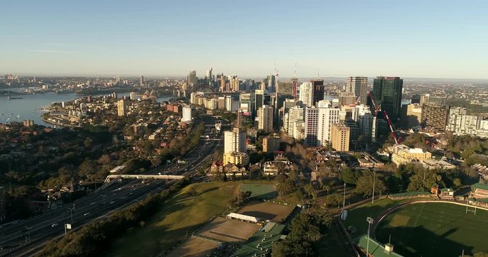 Sports complex and green grass oval in North Sydney along Warringah Freeway in view of distant Sydney city CBD landmarks and high-rise towers.
