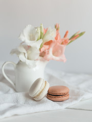 Two pastel French macarons and flowers in a jar on a white background.