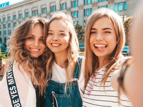 Three young smiling hipster women in summer clothes.Girls taking selfie self portrait photos on smartphone.Models posing in the street.Female showing positive face emotions