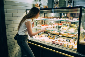 stylish girl with long hair near the window with sweets. chooses cake