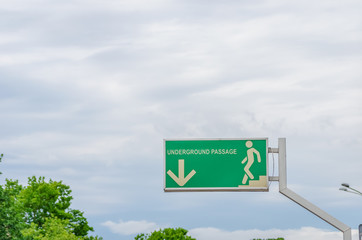 Green road sign indicating the descent into the underpass against the sky and part of the green...