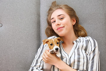 The cutest two months old Jack Russel terrier puppy with beautiful blonde young woman. Small adorable doggy with funny fur stains lying with owner. Close up, copy space, isolated background.