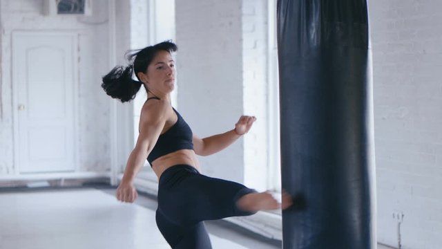 Taekwondo professional athlete woman kicks the punches bag in gym. Athletic Kickboxing woman training in gym.