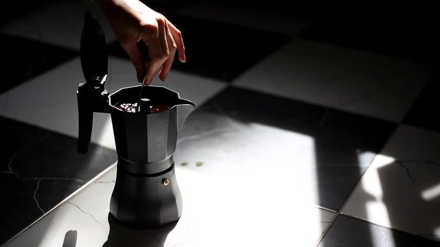 Close-up of female hand who stir coffee in moka pot, on dark background.