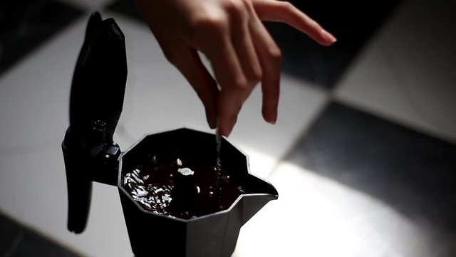 Close-up of female hand who stir coffee in moka pot, on dark background.