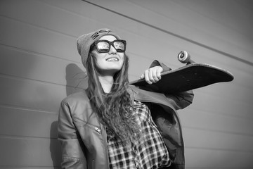 Fototapeta premium A young hipster girl is riding a skateboard. Girls girlfriends for a walk in the city with a skateboard. Spring sports on the street with a skateboard.