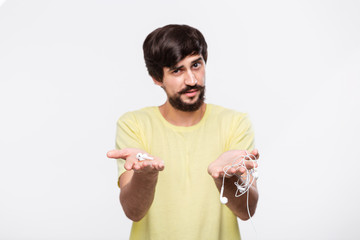 Pretty brunet bearded man with whiskers holds wired headphones in one hand and wireless earbuds in...