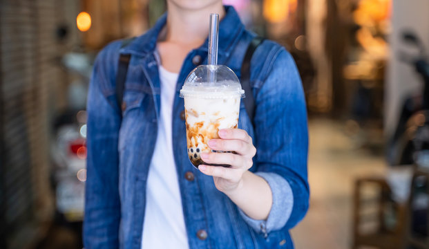 Young Girl In Denim Jacket Is Drinking Brown Sugar Flavored Tapioca Pearl Bubble Milk Tea With Glass Straw In Night Market Of Taiwan, Close Up, Bokeh