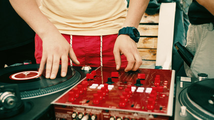 Outdoor party. Dj spinning vinyl record and turning mixer's controllers