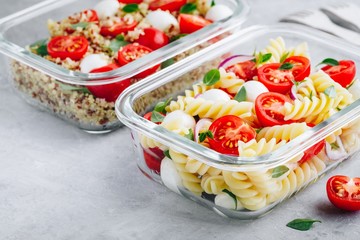 Meal prep containers with pasta salad or quinoa, tomatoes, mozzarella cheese, and basil.