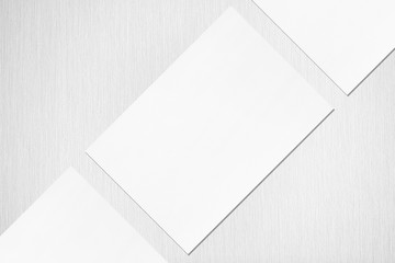 Close up of three empty white rectangle poster or card mockups lying diagonally with soft shadow on neutral light grey textured background. Flat lay, top view. Open composition.