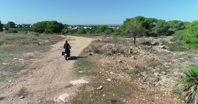 vuelo de dron tras una motocicleta trail gran cilindrada con  maletas, conduciendo en sendero de monta&ntilde;a con piedras