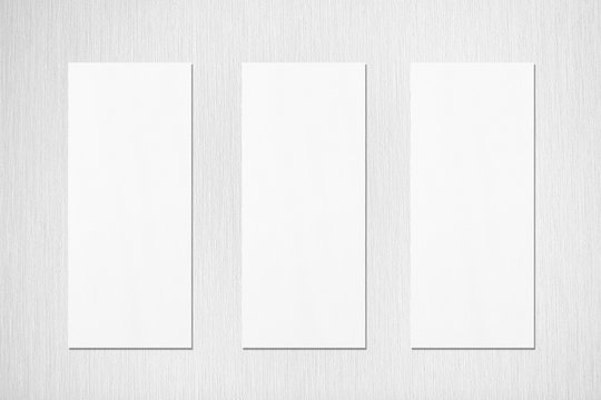 Three empty white vertical rectangle menu mockups with soft shadows on neutral light grey textured wall background. Flat lay, top view
