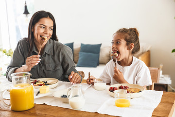 Image of beautiful family mother and little daughter eating together while having breakfast at home...
