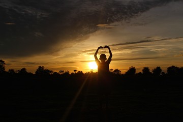 The silhouette of the boy raised his heart-shaped hands and the blue sky, golden yellow sunlight at sunset, taking a blurred photo
