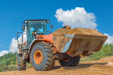 Backhoe loader or bulldozer - excavator with clipping path on a background with blue sky and clouds. work on construction site or sand pit