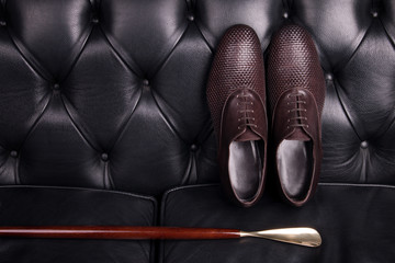 Men brown woven leather shoes and wooden shoe spoon. A pair of handsome men shoes on a black leather sofa.
