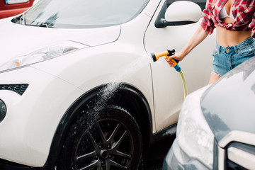 cropped view of girl washing white car while holding pressure washer