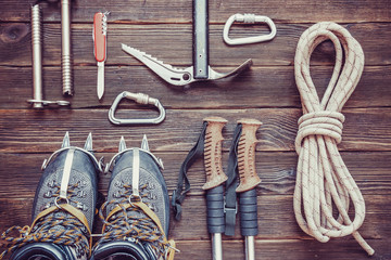 climbing equipment: rope, trekking shoes, crampons, ice tools, ice ax, ice screws, red knife and other set on dark wooden background, top view. Travel concept.