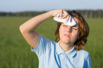 Naklejka premium Unhappy sick young woman suffering from heat, heatstroke in hot warm summer day. Girl sweating drying rubbing her forehead with a handkerchief and fanning. Female feeling bad, having headache outdoor