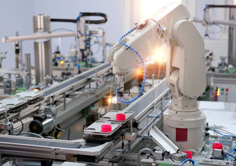 Focus on robotic arm's gripper. Industry 4.0 concept; artificial intelligence in smart factory. Robot picks up the product from automated car on the manufacturing line. Selective focus.