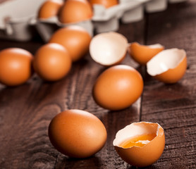 Brown eggs in a box and broken egg with yolk on rustic table.