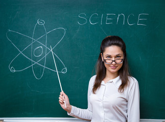 young teacher with glasses talks about science near blackboard